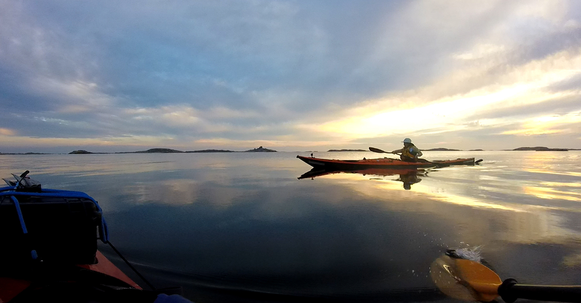 Eine Person fährt mit dem Kajak in einen Sonnenuntergang auf dem Meer.