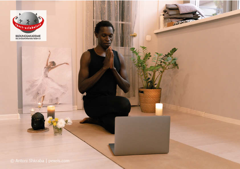 Ein junger Mensch People of colour sitzt vor einem Laptop und praktiziert Yoga Online Achtsamkeit Entspannung