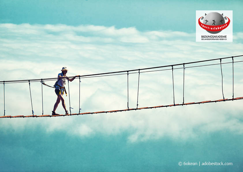 Eine Frau geht abgesichert über eine Hängebrück hoch oben in den Wolken