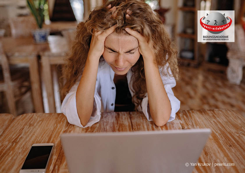 Frau sitzt vor einem Laptop und hält sich bei geschlossenen Augen verärgert den Kopf mit den Händen Selbstmanagement Selbstcoaching Soft Skills Persönlichkeitsentwicklung