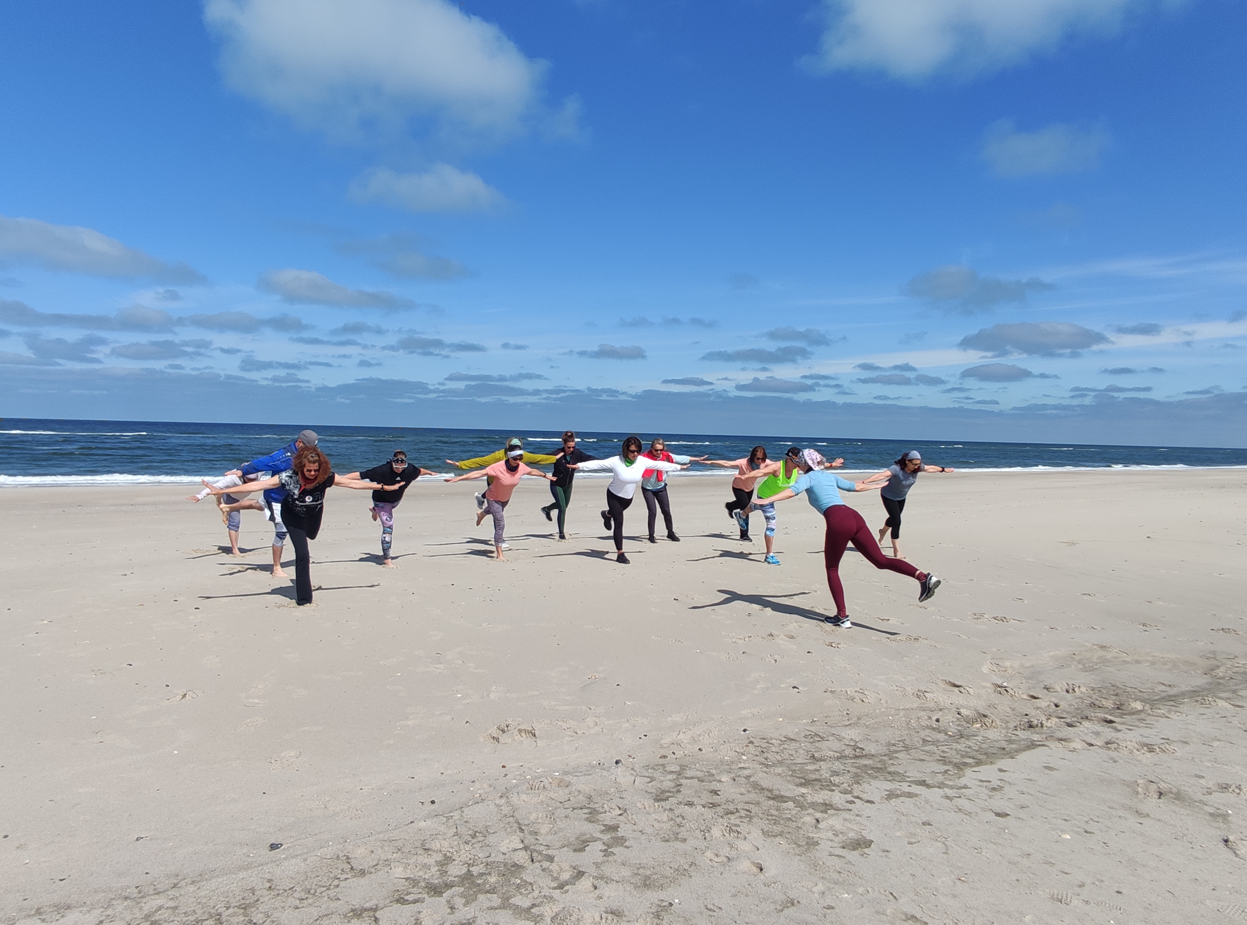 Gruppe trainiert am Strand Gleichgewichtsübungen.