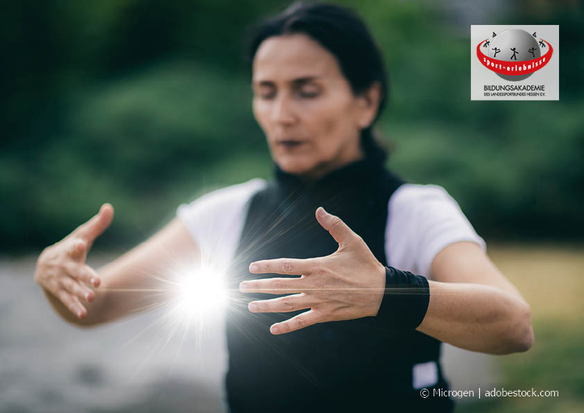 Eine Frau konzentriert beim Qigong-Training. Der Fluss der Energie zwischen ihren Händen leuchtet hell. Bildungsurlaub
