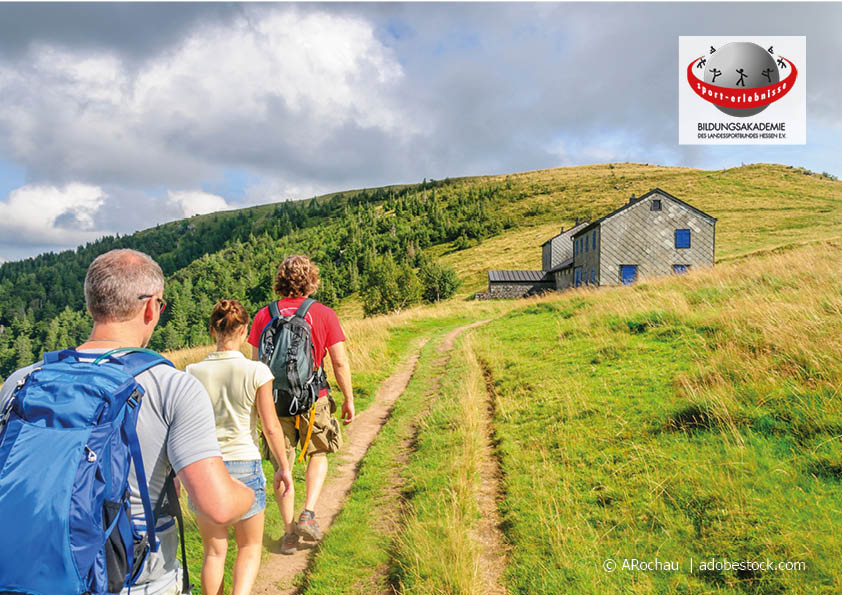 Eine Wandergruppe läuft auf einem Bergweg auf eine Hütte zu bei einem Bildungsurlaub